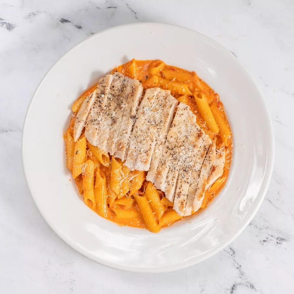Penne pasta in a creamy red sauce topped with sliced grilled chicken and grated cheese.