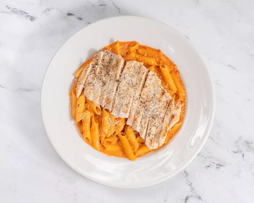 Penne pasta in a creamy red sauce topped with sliced grilled chicken and grated cheese.