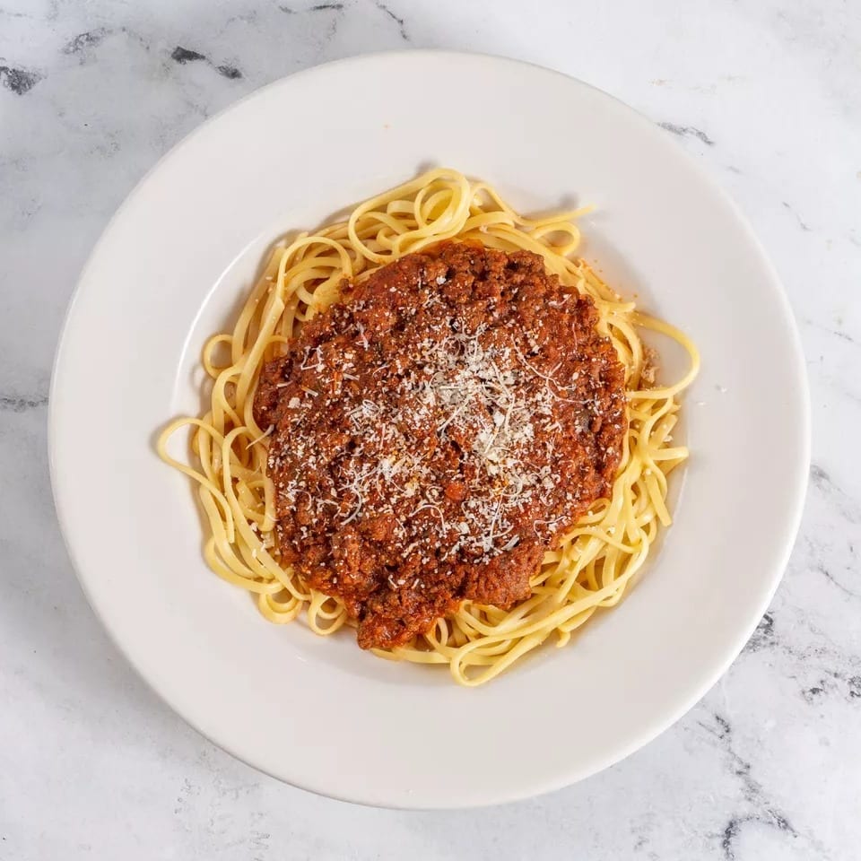 Spaghetti with rich bolognese sauce and grated parmesan cheese on a white plate.