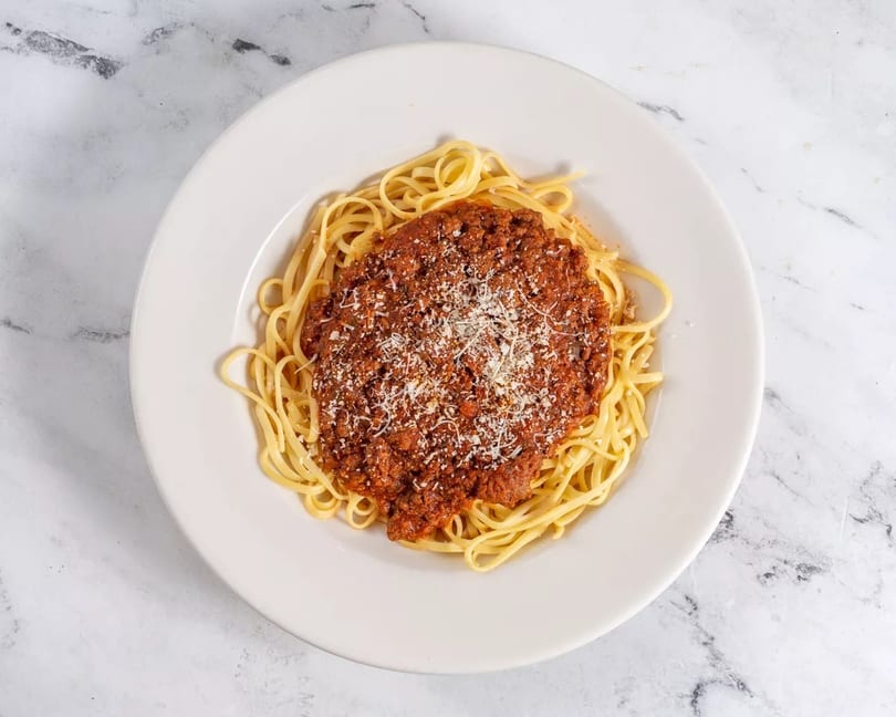 Spaghetti with rich bolognese sauce and grated parmesan cheese on a white plate.