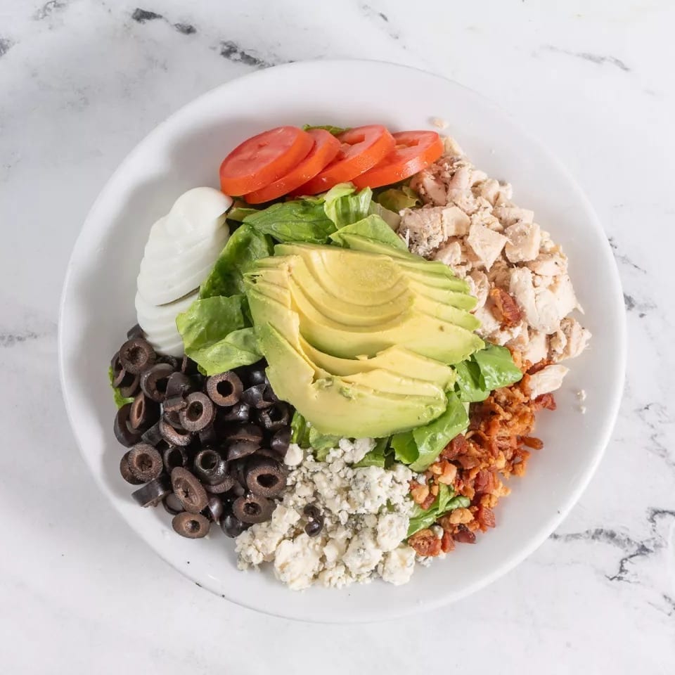 A vibrant Cobb salad with chicken, avocado, bacon, blue cheese, olives, and tomatoes.