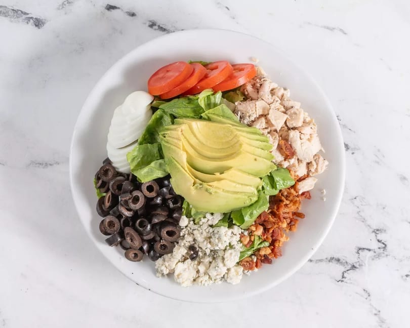 A vibrant Cobb salad with chicken, avocado, bacon, blue cheese, olives, and tomatoes.
