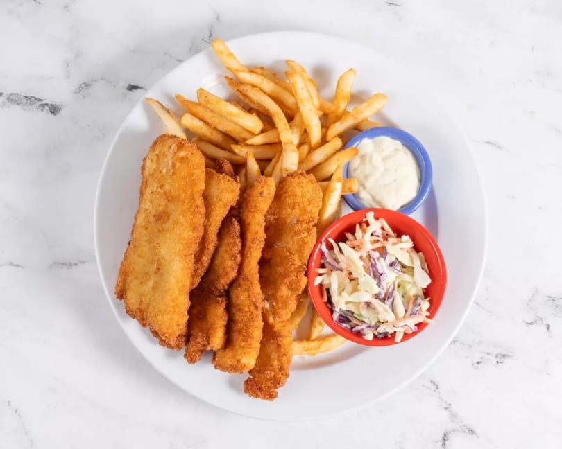 Crispy fried fish fillets and golden french fries with coleslaw and tartar sauce on a white plate.