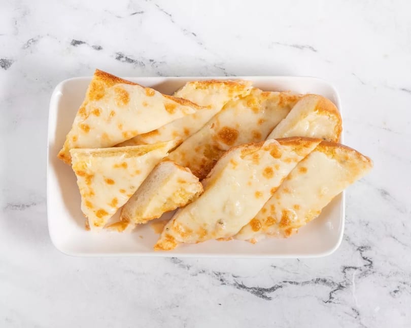 A white rectangular plate filled with golden-brown cheesy garlic bread slices on a marble surface.