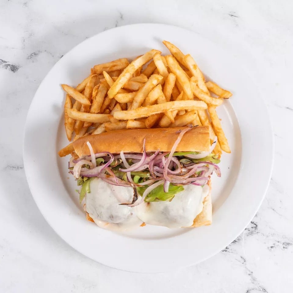 Cheesesteak sandwich with melted cheese, onions, and peppers, served with a side of french fries.