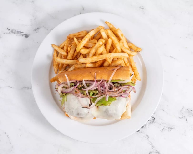 Cheesesteak sandwich with melted cheese, onions, and peppers, served with a side of french fries.
