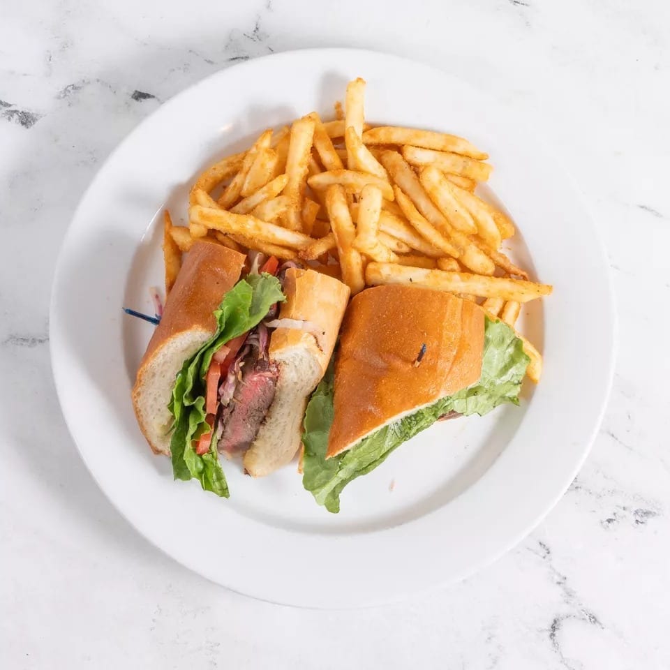 Steak sandwich with lettuce, tomato, and onions, served with a side of golden french fries.