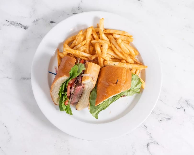 Steak sandwich with lettuce, tomato, and onions, served with a side of golden french fries.