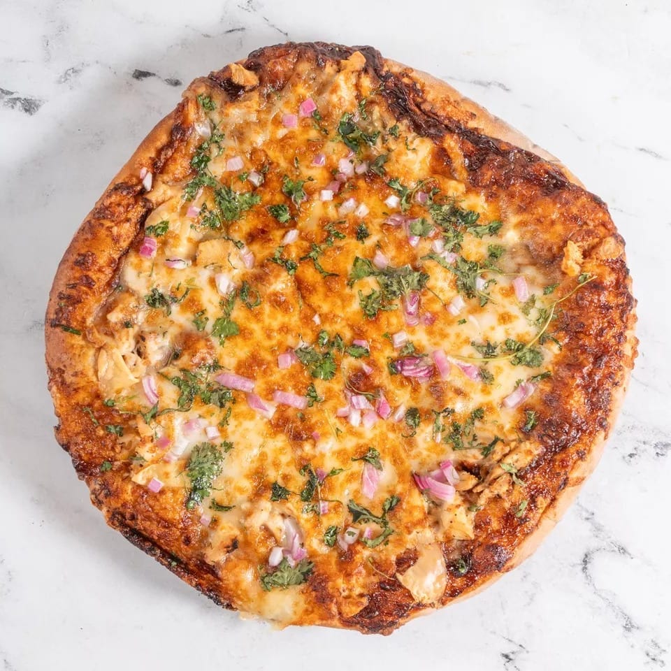 A golden-crusted pizza topped with melted cheese, red onions, and fresh cilantro on a marble surface.
