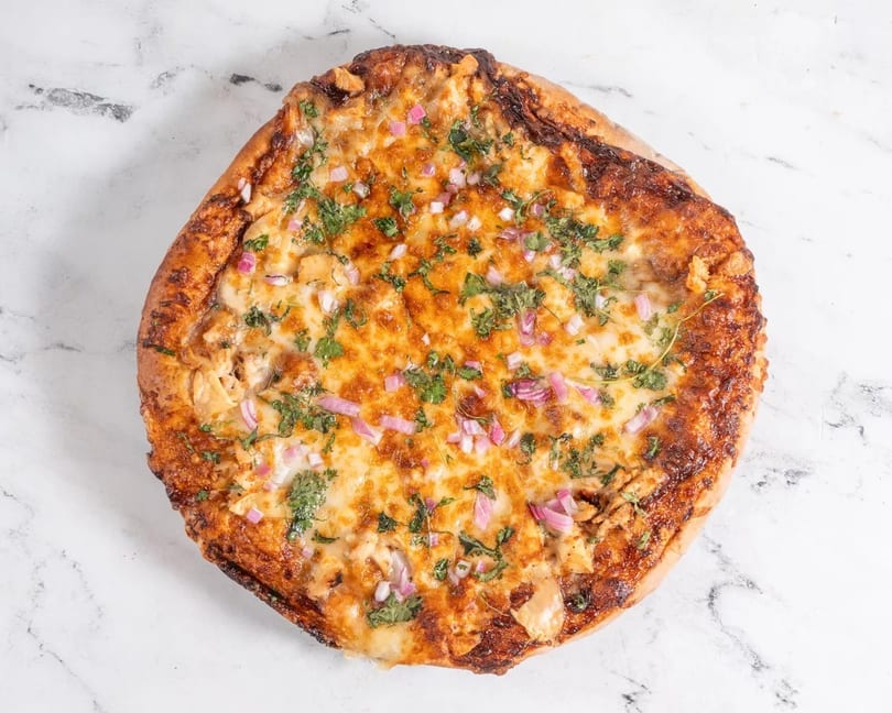 A golden-crusted pizza topped with melted cheese, red onions, and fresh cilantro on a marble surface.